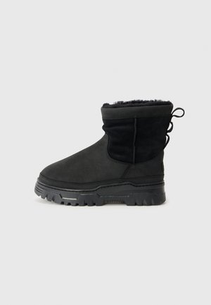 Black suede ankle boots with a soft fur lining and thick, rugged soles, featuring a pull tab at the back for easy wear.