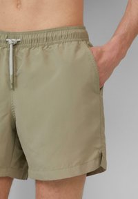 Khaki plavky vyrobené z ľahkého materiálu, s elastickým pásom na šnúrku a bočnými vreckami. Jednoduchý, funkčný dizajn.