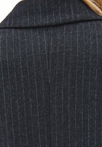 Blazer gris carbón con patrón de pinstripes, confeccionado en tejido texturizado. Presenta un cuello de muesca y un corte limpio y ajustado.