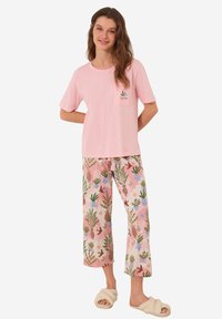 T-shirt in cotone rosa con taschino sul petto; pantaloni del pigiama abbinati presentano un motivo di piante colorate su fondo rosa; pantofole pelose.