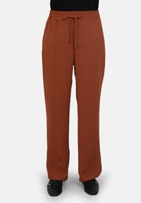 Pantalons bruns amples en tissu doux. Dotés d'une taille élastique avec un lien et d'une coupe droite. Évasés en bas.