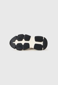 Semelle en caoutchouc noire avec des motifs de texture antidérapants et une intercalaire ivoire. Comprend des sections distinctes pour la flexibilité et la traction.