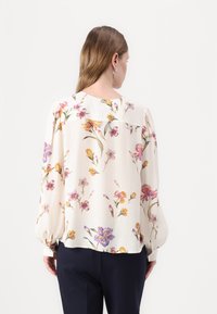 Kreminė gėlių blusas su ilgomis, plačiomis rankovėmis; su daugiaspalvėmis gėlėmis violetinės, geltonos ir rožinės spalvų; apvalus iškirpimas, lengvas audinys.