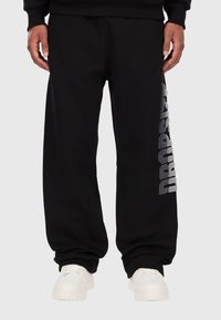 Schwarze Sporthose mit lockerer Passform, ausgestattet mit einem silbernen "DROPSIZE"-Grafik auf dem linken Bein und gerippten Bündchen an den Knöcheln.