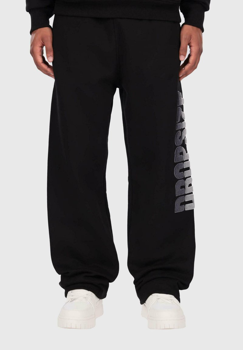 Schwarze Sporthose mit lockerer Passform, ausgestattet mit einem silbernen "DROPSIZE"-Grafik auf dem linken Bein und gerippten Bündchen an den Knöcheln.