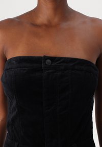 Svart strapless topp i mjukt tyg med framknäppning, subtil textur och sömdetaljer. Inga mönster eller dekorationer synliga.