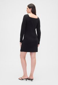 Svart langermet kjole med firkantet utringning, tettsittende silhuett og knelengde.