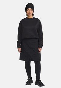 Felpa nera con colletto tondo, gonna nera trapuntata, leggings neri e berretto nero testurizzato. Indossato con scarpe da ginnastica nere.