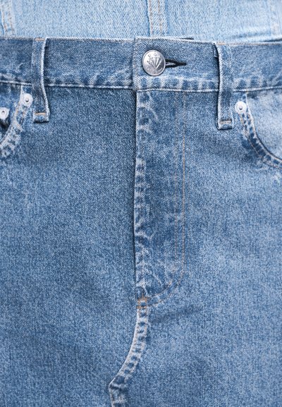 Κοντινό πλάνο στη μέση από τζιν παντελόνι ανοιχτού μπλε χρώματος με ασημί κουμπί, θηλιές για ζώνη και εμφανές ράψιμο μπροστινών τσεπών.