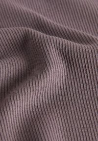 Primer plano de tela textil suave y acanalada en púrpura polvoriento con líneas verticales de punto visibles y pliegues suaves que crean textura.