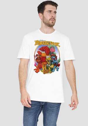 Man wearing white t-shirt with colorful Fraggle Rock characters and logo on front, paired with blue jeans, on gray background.