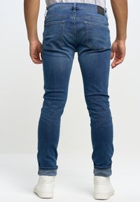 Modré džíny se slim fit střihem, s středním pasem, ohrnutými manžetami a dvěma zadními kapsami. Kombinováno s bílými teniskami.