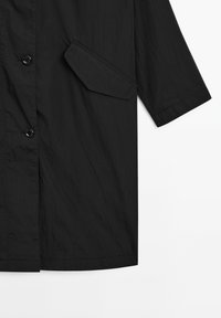 Černá lehká bunda s krumplem, zapínáním na knoflíky, boční kapsou s ostrým tvarem a rukávy o délce tři čtvrtě.