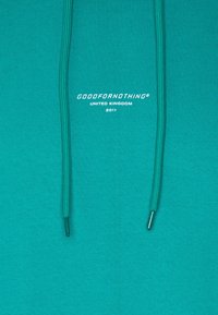 Sudadera verde azulado con dos cordones y texto blanco "GOODFORNOTHING UNITED KINGDOM 2011" en el centro del frente.