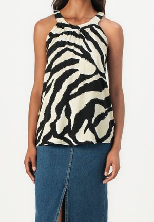 Femme portant un haut sans manches à imprimé zèbre noir et blanc avec un col froncé et une jupe en denim bleue avec une fente à l'avant.