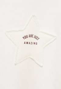 Bílá tkanina s nášivkou ve tvaru hvězdy se zvýšeným prošíváním. Nášivka obsahuje text "JSTE JEN ÚŽASNÍ" v bordó.