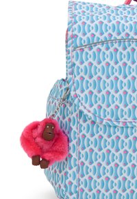 Blauer Rucksack mit einem geometrischen Muster in hellen und dunklen Farbnuancen. Enthält einen pinken, pelzigen Affen-Schlüsselanhänger mit einem braunen Gesicht, der mit einem Kettenanhänger befestigt ist.