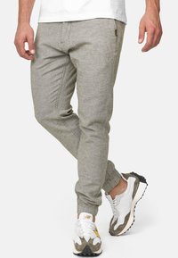 Pantalones jogger de color gris claro con una tela texturizada, con puños elásticos y un corte ajustado, combinados con zapatillas deportivas blancas y grises.