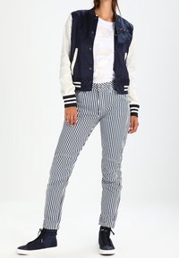 Mörkblå satin bomberjacka med krämfärgade ärmar, vit grafisk t-shirt, randiga mörkblå byxor och mörkblå högskor.