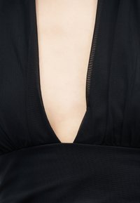 Κοντινό πλάνο βαθιού ντεκολτέ σχήματος V σε μαύρο ένδυμα που αποκαλύπτει το δέρμα κάτω από ελαφρύ, ελαφρώς διάφανο ύφασμα.