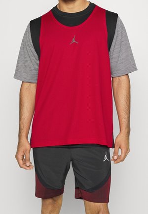 Mand iført lag på lag af sort og grå T-shirt, rød ærmeløs sportstrøje og sorte og røde atletikshorts med Jumpman-logoer.