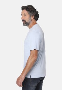 Camiseta de algodón de color azul claro con mangas cortas, cuello redondo y corte recto, con aberturas laterales para mayor comodidad. Llevada con jeans oscuros.