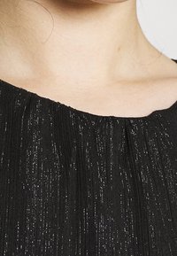 Schwarzer, strukturierten Stoff mit feinen, schimmernden Fäden und vertikalen Falten. Verfügt über einen bescheidenen, leicht geschwungenen Ausschnitt und eine glatte Oberfläche.