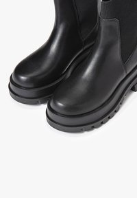 Svarta lädersstövlar med slät yta, tjock gummisula och elastiska sidopaneler för enkel påtagning. Har en robust, minimalistisk design.