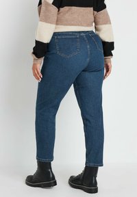 Tmavě modré džíny s rovným střihem a dvěma zadními kapsami, spárované s černými botami. Vypadá opotřebovaně s barevným pruhovaným svetr.