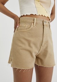 Beige denim shorts med frynset kant, med høj talje, sidelommer og syede detaljer nær lommekanterne.