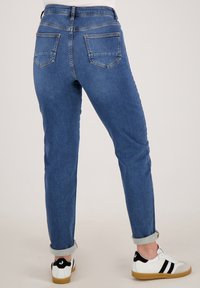 Blauwe denim jeans met een fitted silhouet, met een hoge taille, opgerolde pijpen en twee achterzakken. Draagt met witte sneakers.