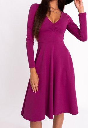 Długa sukienka z długim rękawem w kolorze fuksji, z dekoltem w serek, marszczeniem na wysokości biustu, rozkloszowanym dołem w kształcie litery A oraz miękkim, elastycznym materiałem.
