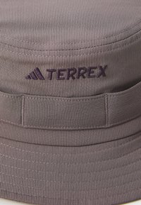 Grå bøttehat med ribbet tekstur, der har et broderet lilla "TERREX" logo og et vandret bånd til justering.