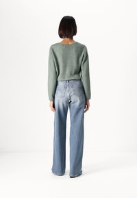 Grön stickad tröja med v-ringning och långa ärmar, kombinerad med ljusblå, blekta vida jeans. Bakgrunden är helt vit.