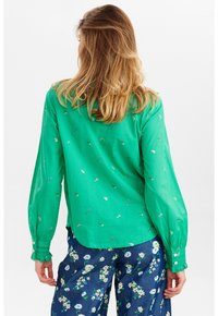 Camicia verde a maniche lunghe con ricami floreali e polsini abbottonati, abbinata a pantaloni scuri con motivo floreale. Tessuto morbido e leggero.