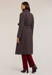 Cappotto lungo bordeaux e bianco con motivo a disegno, completo di cintura, colletto classico, tasche laterali e una vestibilità elegante e su misura. Abbinato a pantaloni bordeaux.