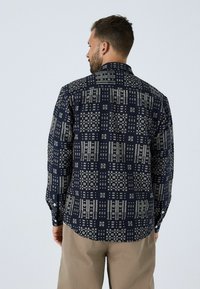 Tumes sinine mustriga särk, millel on struktureeritud krae, pikad varrukad ja nööpidega tagaosa; sellel on geomeetrilised kreemjad mustrid ja sile tekstuur.