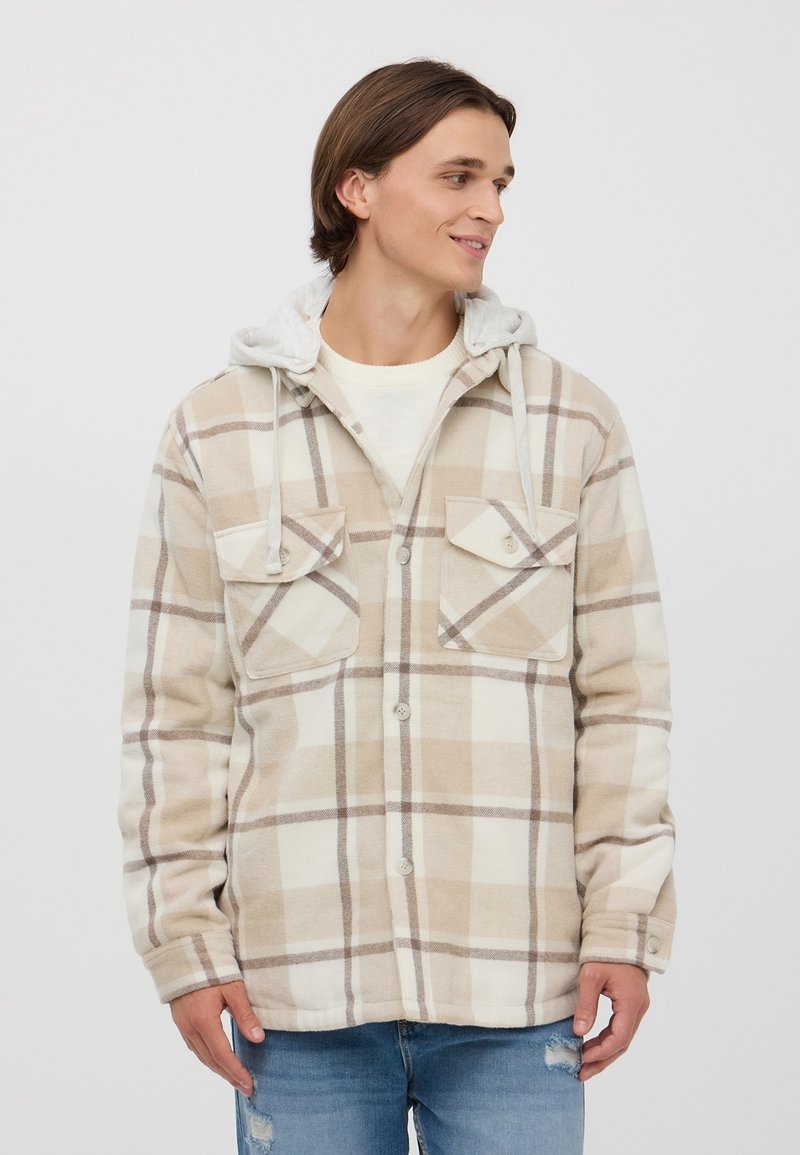 Giacca di flanella a quadri beige con cappuccio grigio, caratterizzata da un frontale con bottoni, due tasche sul petto e una texture morbida.