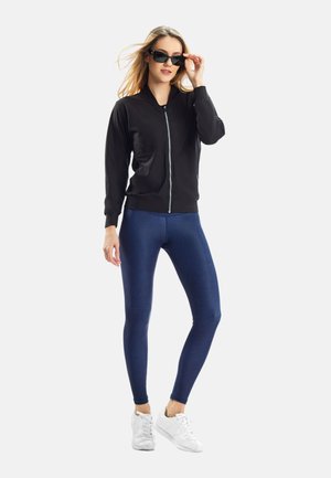 Schwarze Zip-Jacke, blaue Leggings und weiße Sneakers. Glattes Material, taillierte Passform, abgerundete Bündchen und eine elegante Silhouette.