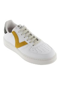 Zapatilla blanca con un acento texturizado amarillo y talón negro. Presenta una puntera perforada y cordones gris claro sobre una suela de goma.
