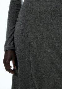 Graues langärmliges Kleid mit weichem Stoff, schmaler Passform und einem seitlichen Nahtdetail, das in der Nähe einer Hand sichtbar ist. Das Material scheint gestrickt zu sein.