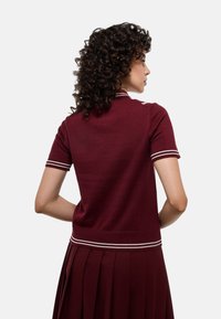 Polo en tricot bordeaux à manches courtes, avec un col à rayures blanches et un ourlet côtelé ; texture lisse et coupe ajustée.