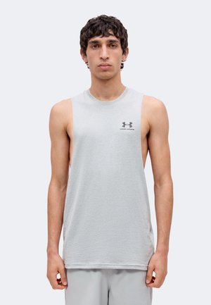 Mladý muž s krátkymi kučeravými vlasmi, oblečený v svetlosivom tielku bez rukávov značky Under Armour a svetlosivých krátkych nohaviciach, pozerá sa dopredu na jednoduchom pozadí.