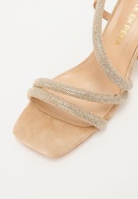 Sandales beiges à talons avec des brides en strass scintillants, bout carré et texture en daim doux. Présente un design minimaliste avec des accents élégants.