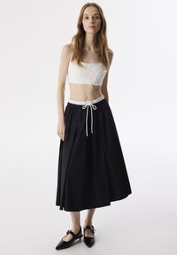 Witte textuur crop top met een vierkante halslijn, gecombineerd met een lange zwarte rok met een elastische tailleband en koord. Zwarte puntige schoenen.