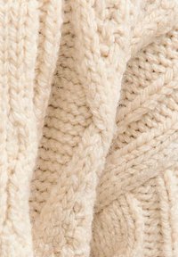 Dikke gebreide beige trui stof met textuurpatronen, die dikke, verweven garens laat zien en een zachte, pluizige uitstraling heeft.