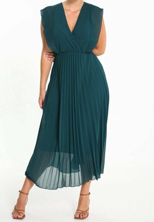 Ærmeløs mørkegrøn plisseret midi-kjole med V-hals og flæseærmer, båret med brune, remmede høje hæle.