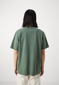 Zielona bawełniana koszulka z krótkim rękawem i okrągłym dekoltem. Charakteryzuje się luźnym krojem i gładką fakturą. Brak widocznych wzorów i akcentów.