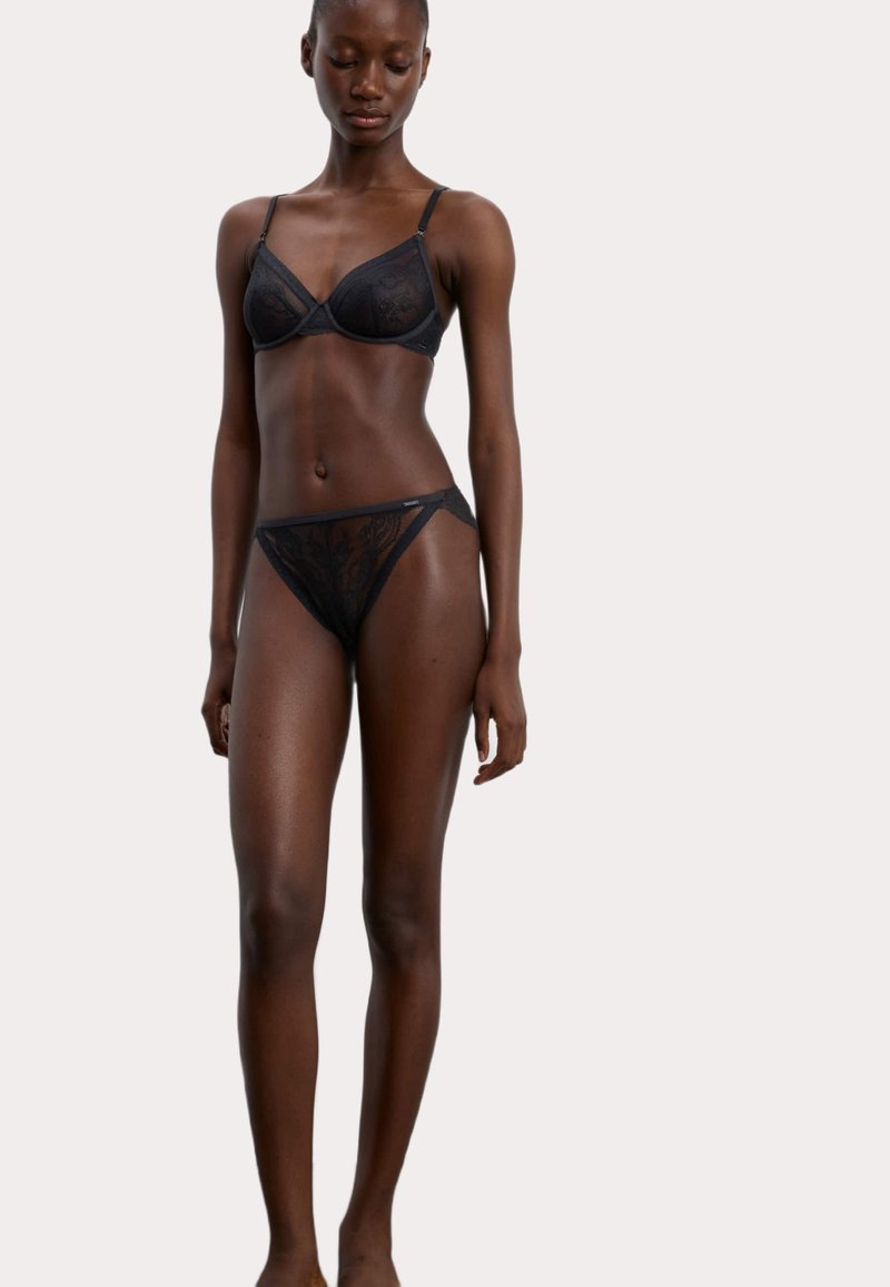 Ensemble en dentelle noire comprenant un soutien-gorge et un string, ornés de motifs floraux délicats, de bretelles ajustables et d'une texture transparente. Coupe élégante et matériel minimal.