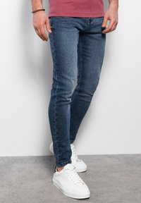 Jeans skinny azules con una textura de denim suave, que cuentan con un diseño clásico de 5 bolsillos. Combinados con zapatillas bajas blancas.